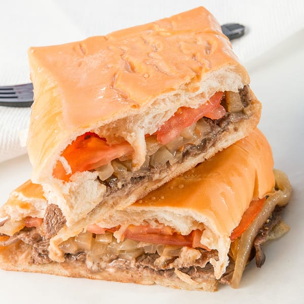 Two halves of a Cubano Bros sandwich filled with steak, onions, and tomatoes.
