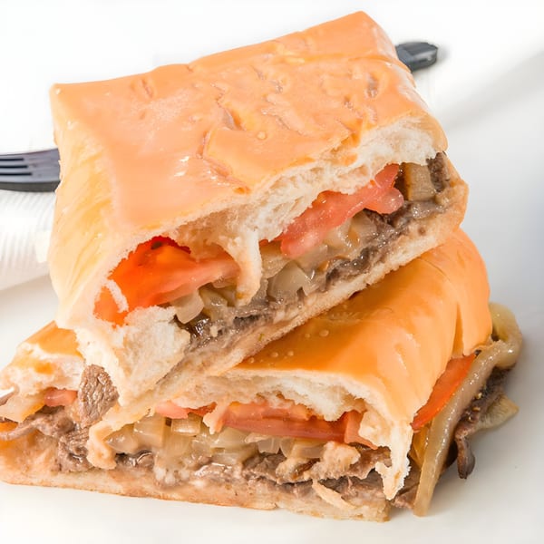 Two halves of a Cuban sandwich with steak, onions, tomatoes, and melted cheese.