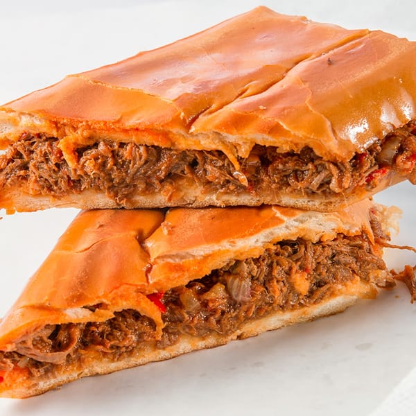 Two halves of a Cubano Bros Cuban sandwich, revealing savory shredded meat and onions.