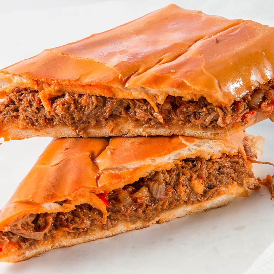 Two halves of a Cubano Bros Cuban sandwich, revealing savory shredded meat and onions.