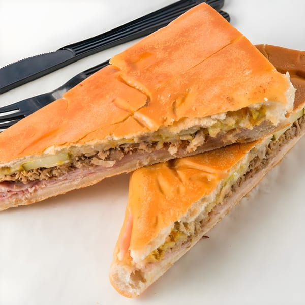 Two halves of a Cubano sandwich, filled with ham, roasted pork, Swiss cheese, pickles, and mustard.