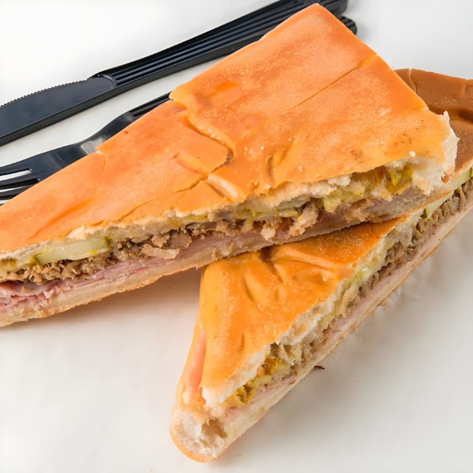 Two halves of a Cubano sandwich, filled with ham, roasted pork, Swiss cheese, pickles, and mustard.