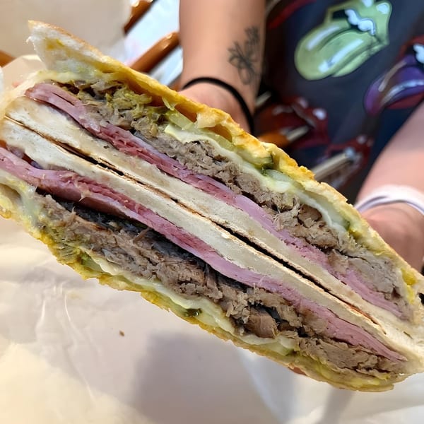 Close-up of a Cubano Bros Cuban sandwich, cut in half, revealing layers of meat, cheese, and pickles.