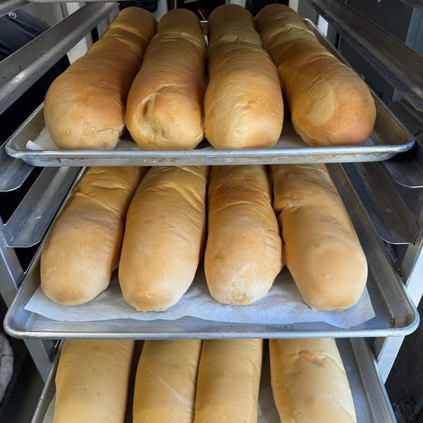 Freshly baked Cuban bread loaves on metal trays, ready for Cubano Bros sandwiches.