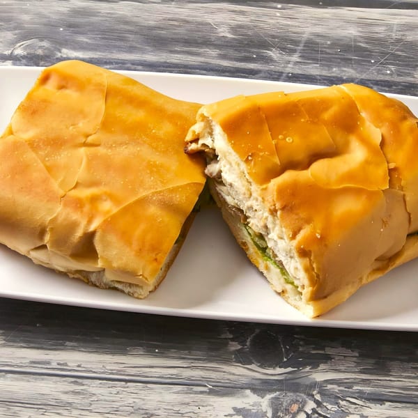 A Cubano Bros sandwich, cut in half, revealing meat, cheese, and green filling on a white plate.