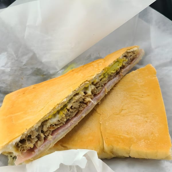 A Cubano Bros Cuban sandwich, cut in half, revealing ham, roasted pork, Swiss cheese, pickles, and mustard.